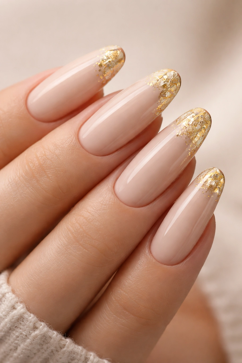 Close-up of long round acrylic nails in beige with gold foil accents