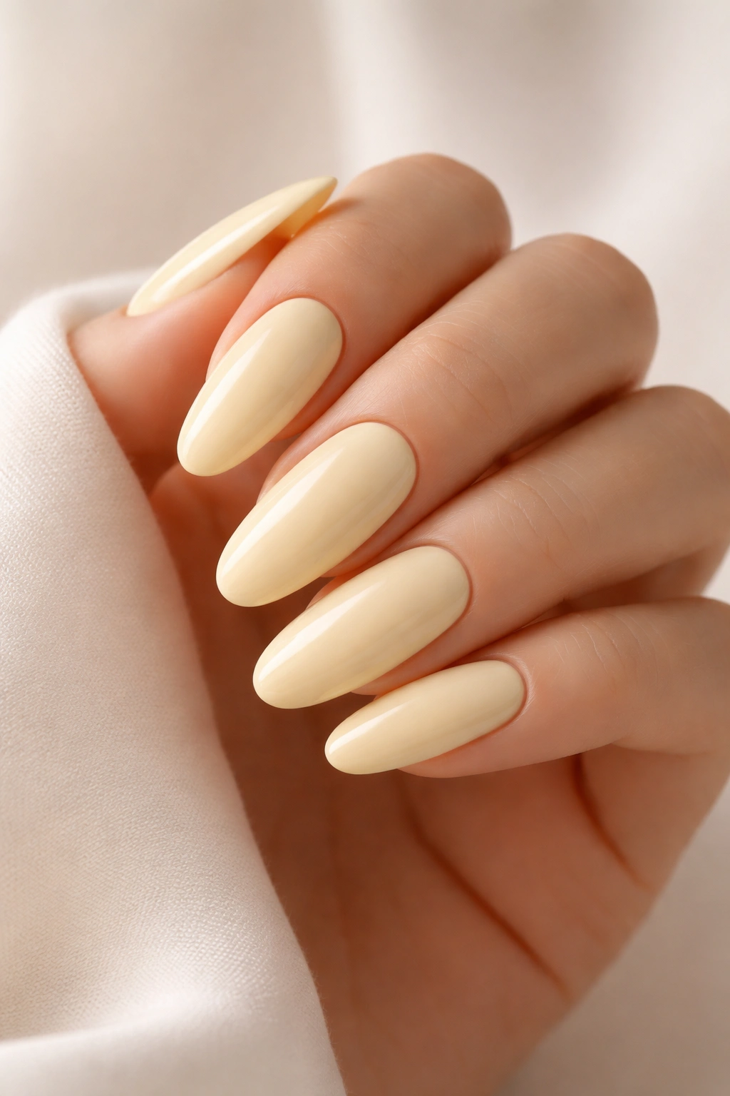 Close-up of long round acrylic nails in pale yellow soft shade with glossy finish