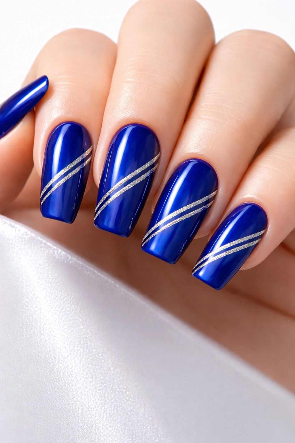 Close-up of royal blue nails with thin silver stripes in a minimalist geometric design
