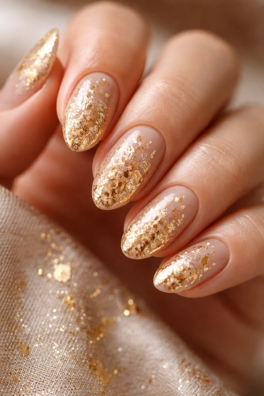Close-up of warm beige nails with gold leaf glitter flecks