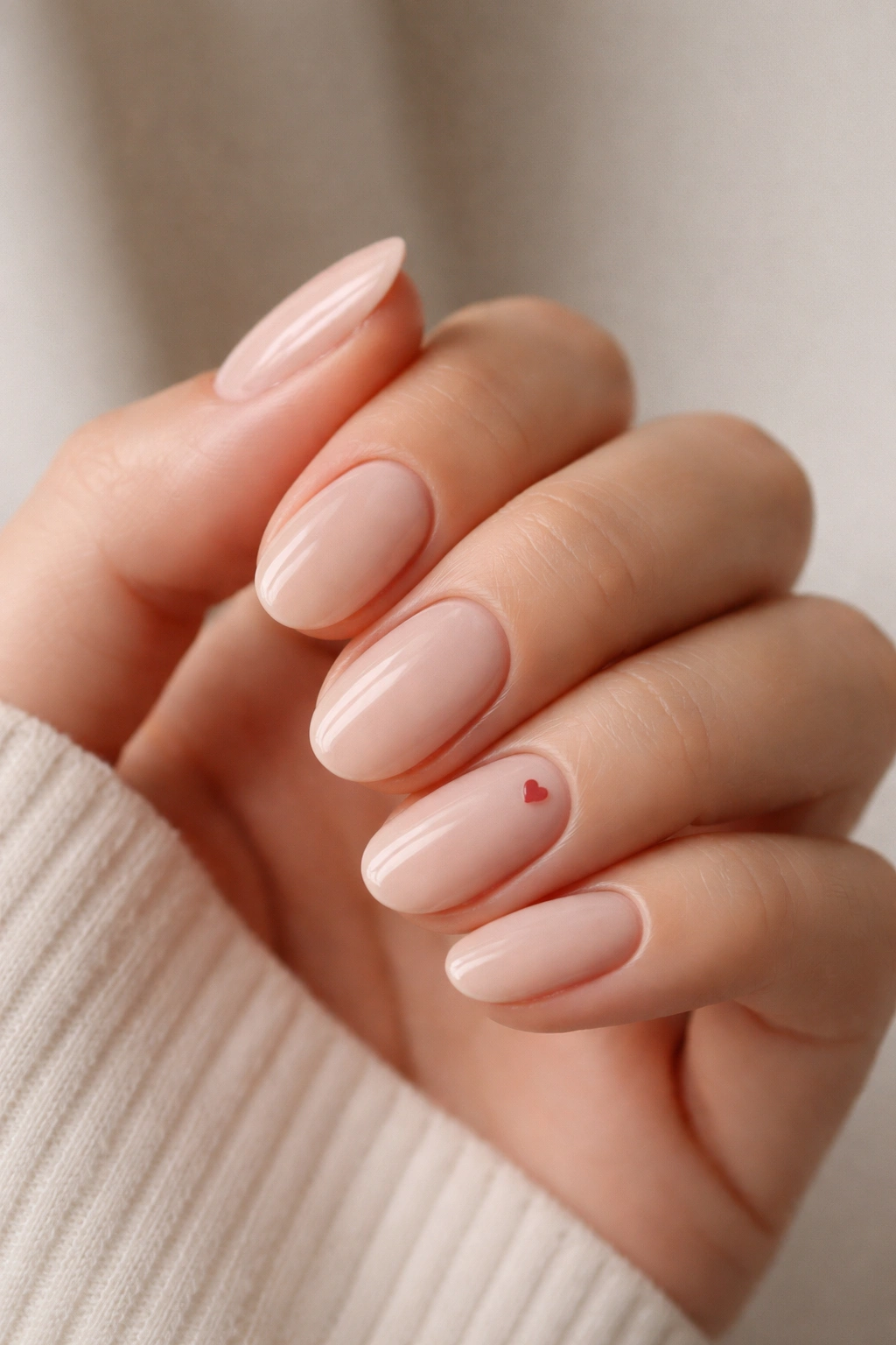 Close-up of nude base short oval acrylic nails with a single slim heart accent