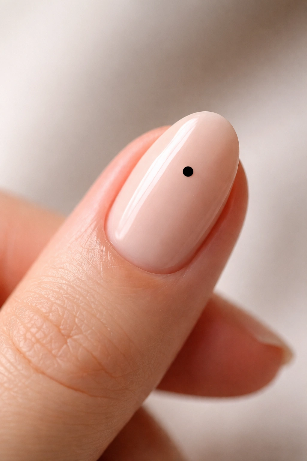 Close-up of nude oval nail with a tiny black dot near the cuticle