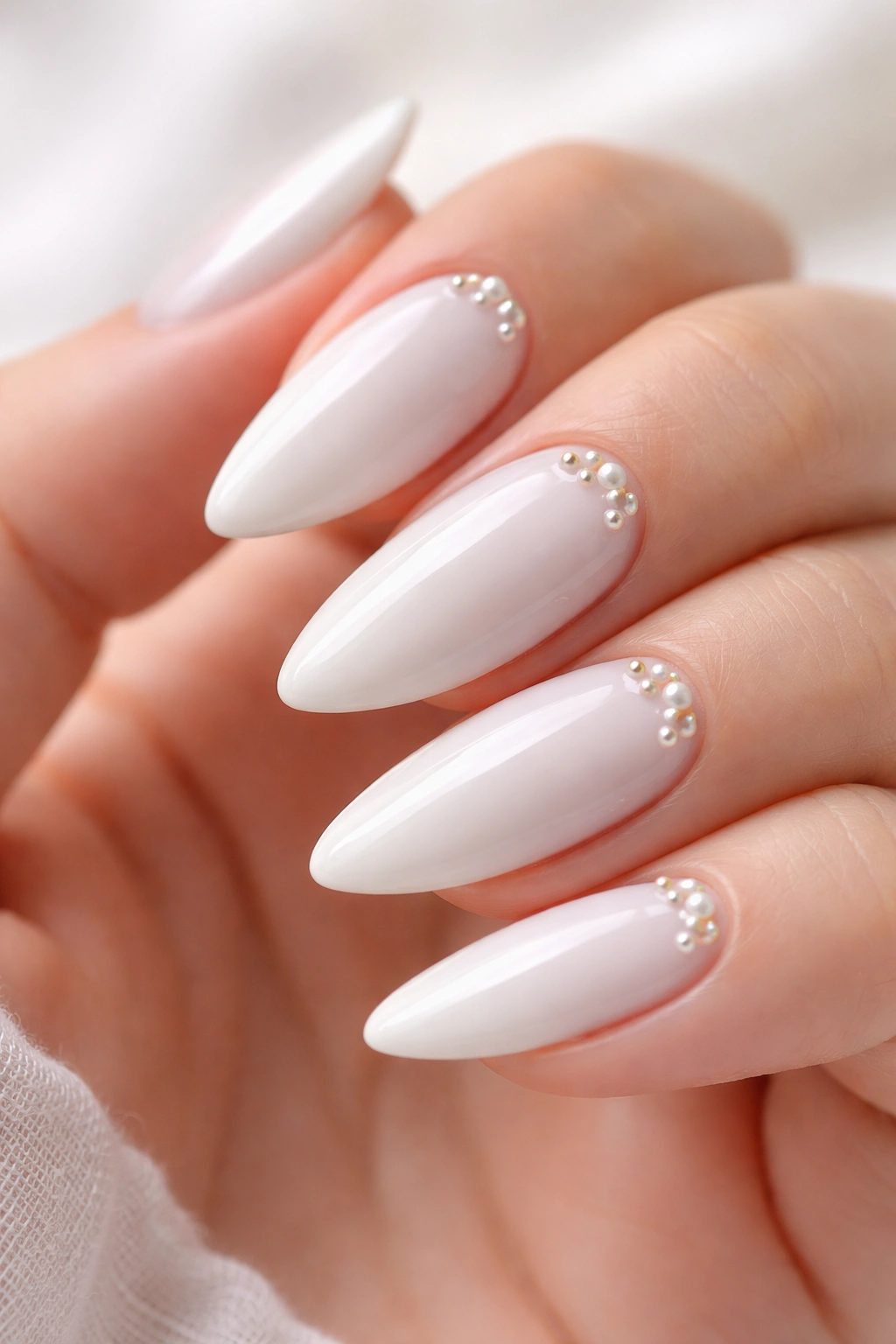Close-up of white almond nails with tiny pearl accents near the cuticle