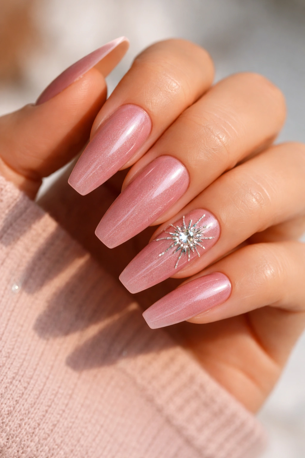 Close-up of pink cat-eye nails with a starburst crystal accent on the ring finger