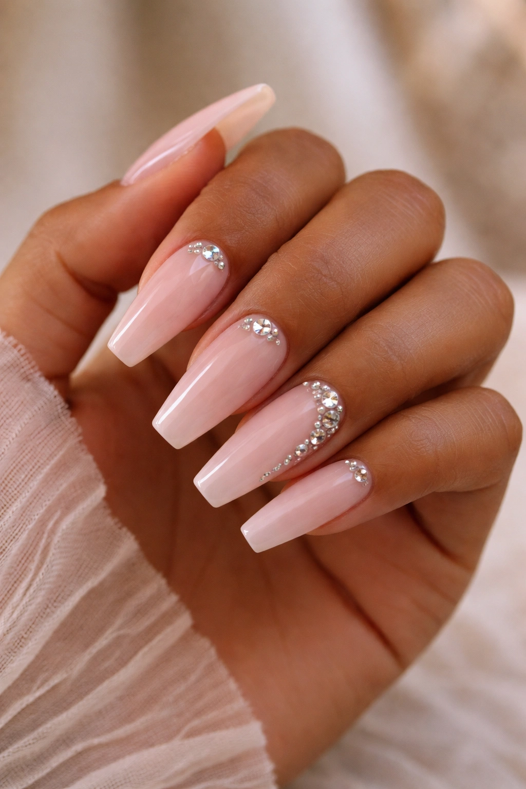 Close-up of warm-skin-toned hand with creamy pink-based pink rhinestone ballerina nails.