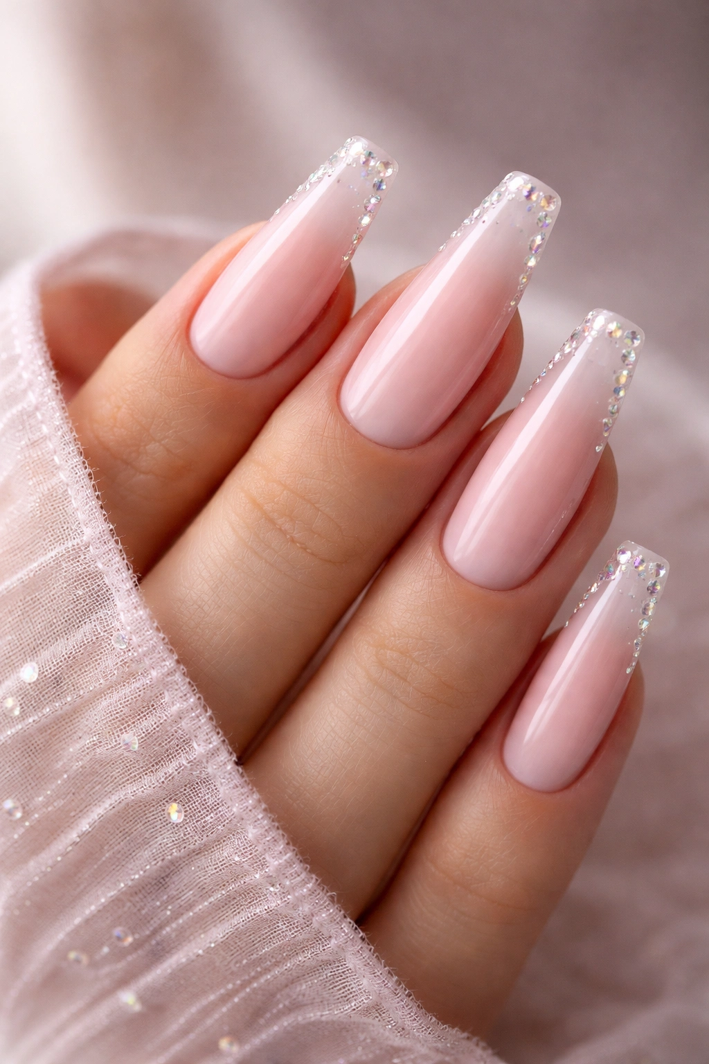 Close-up of pink milky-base rhinestone ballerina nails with crystal accents on tapered nails.
