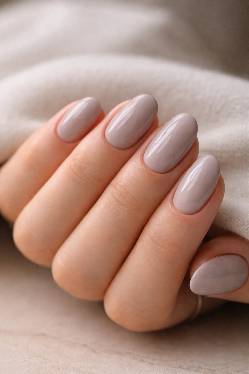 Close-up of short oval acrylic nails in soft grey nude with beige-mauve undertones on a hand