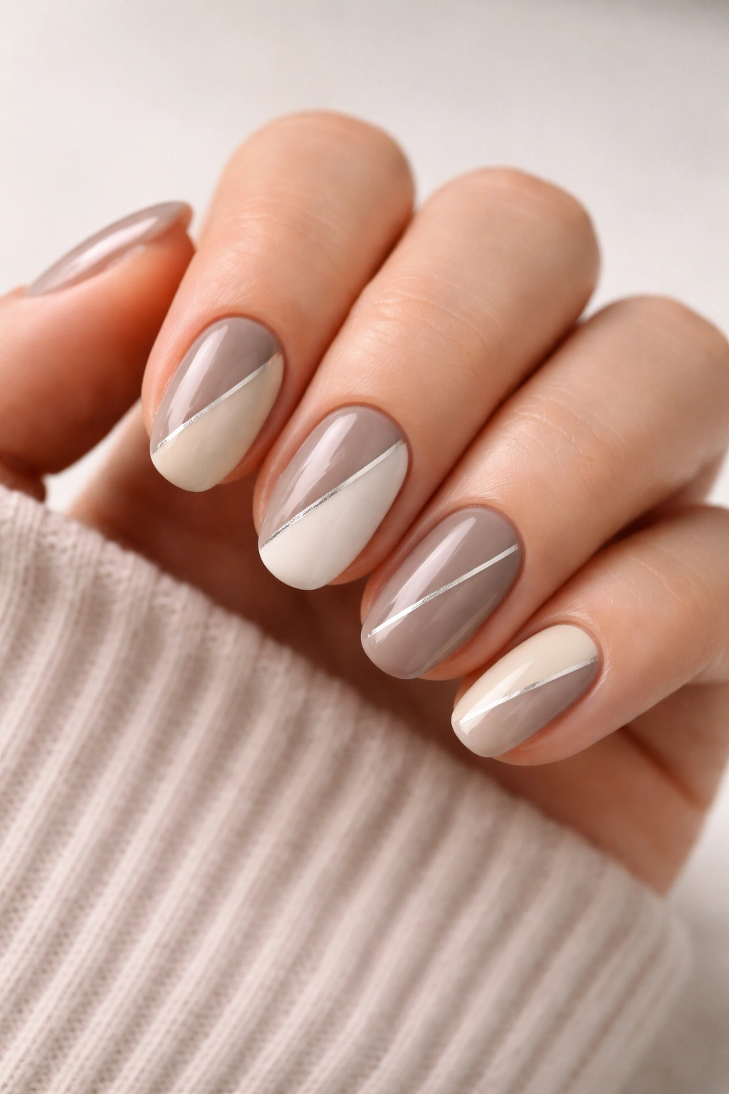 Close-up of short oval nails with taupe and cream color block split by a thin line