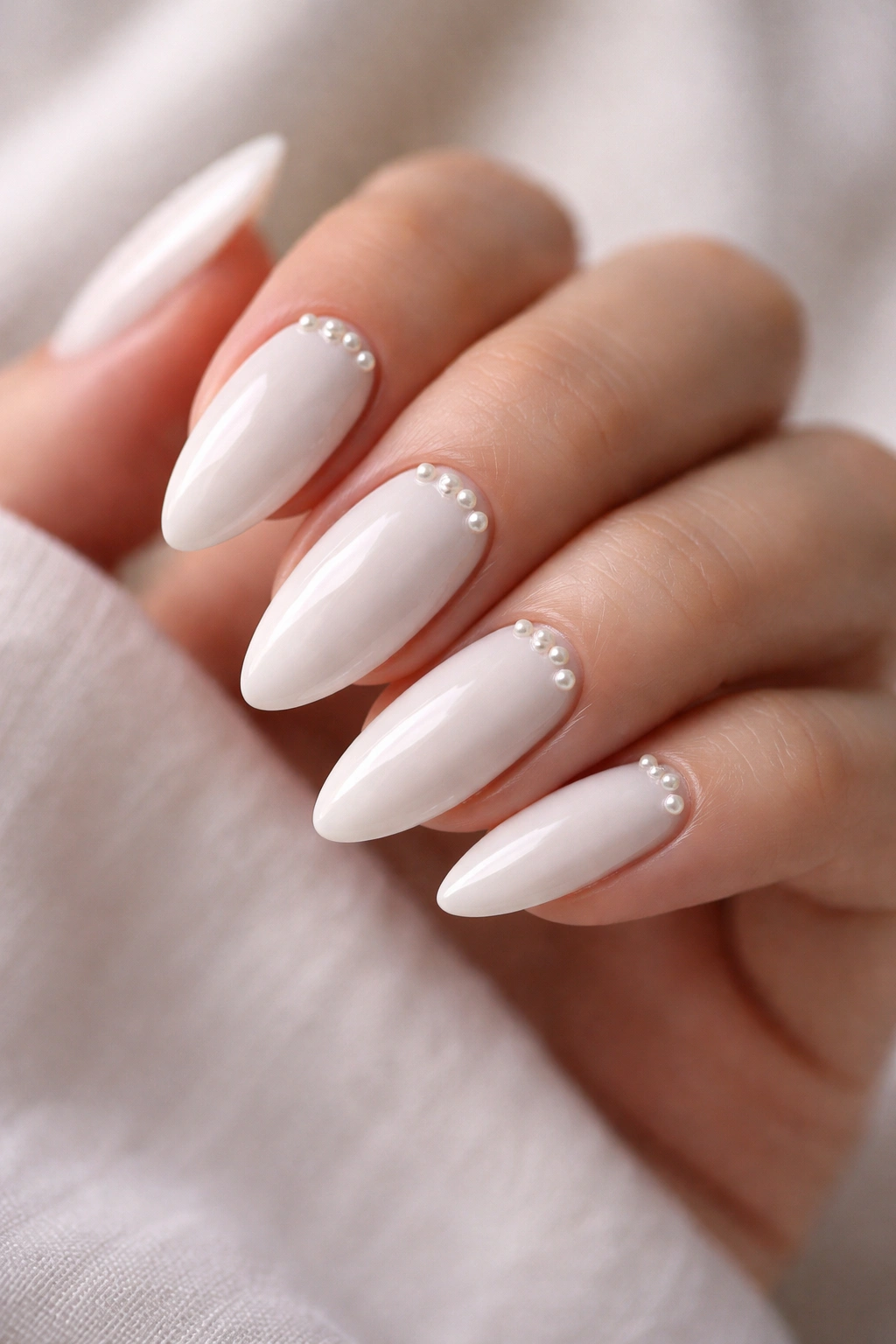 Close-up of white almond nails with tiny pearls on a glossy base