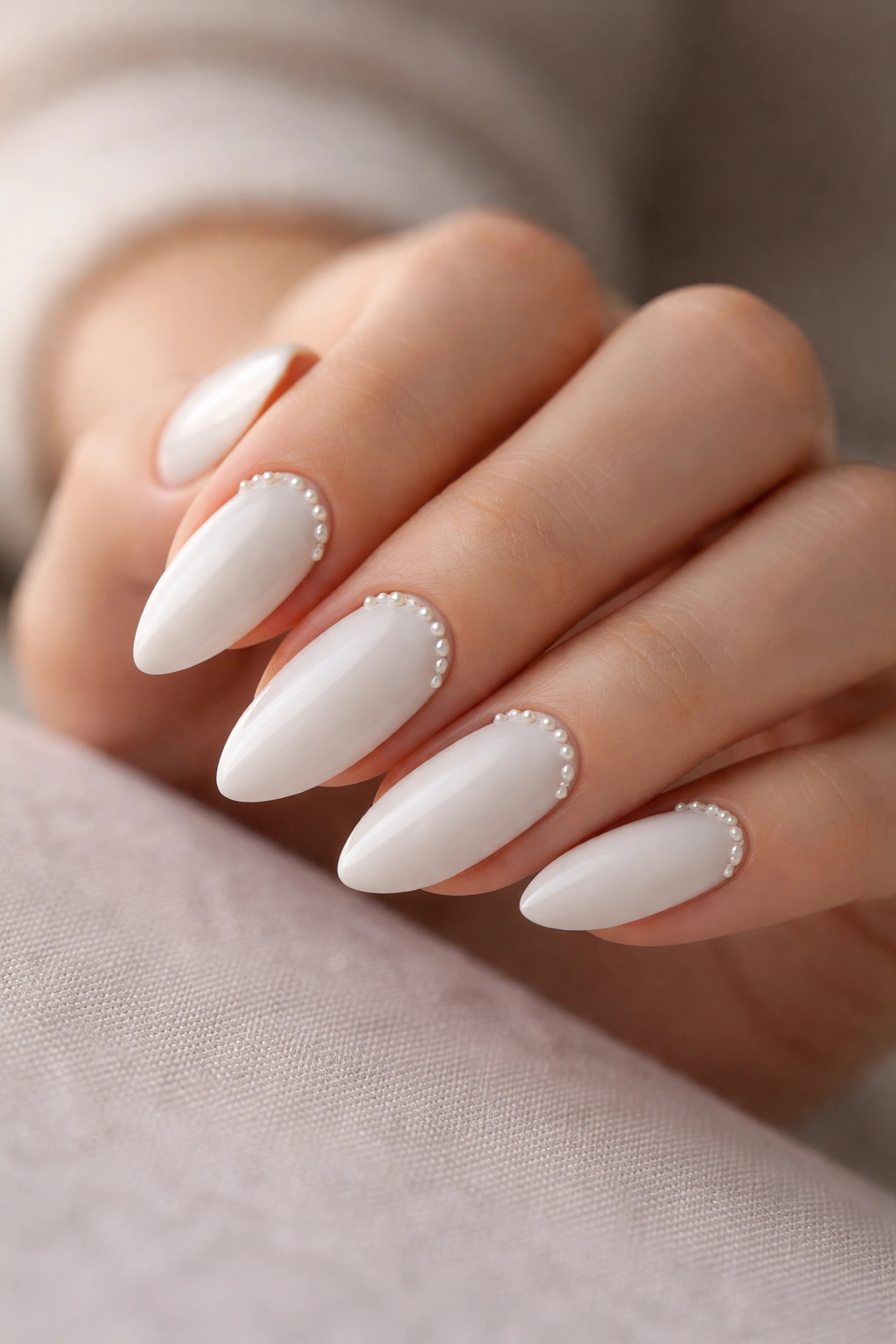 Close-up of white almond nails with tiny pearls near the cuticle on a glossy white base