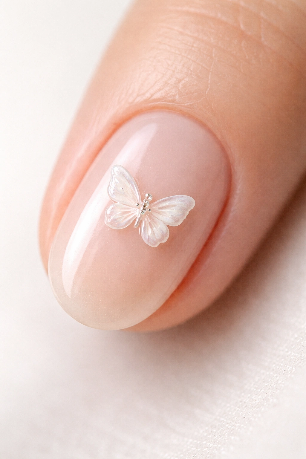 Close-up of a short oval nail with a 3D butterfly appliqué on a sheer nude base