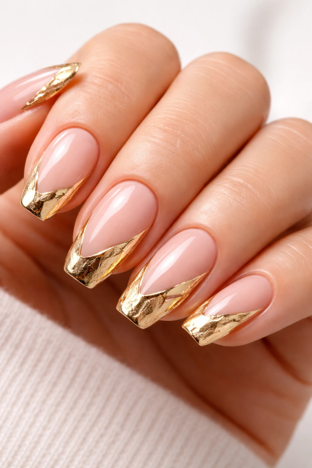 Close-up of abstract gold French tips on nude nails with irregular shapes
