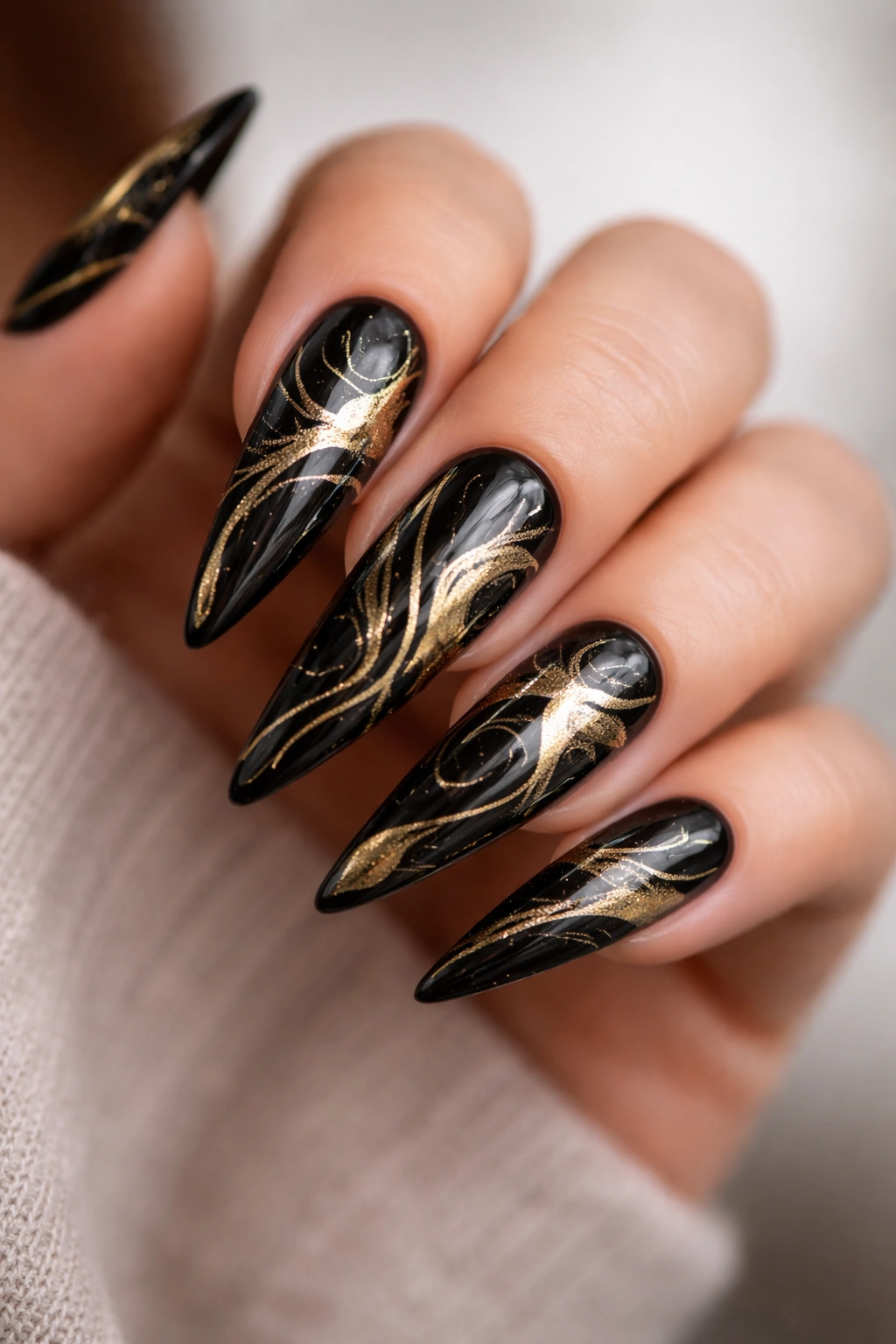 Close-up of black stiletto nails with irregular gold abstract lines.