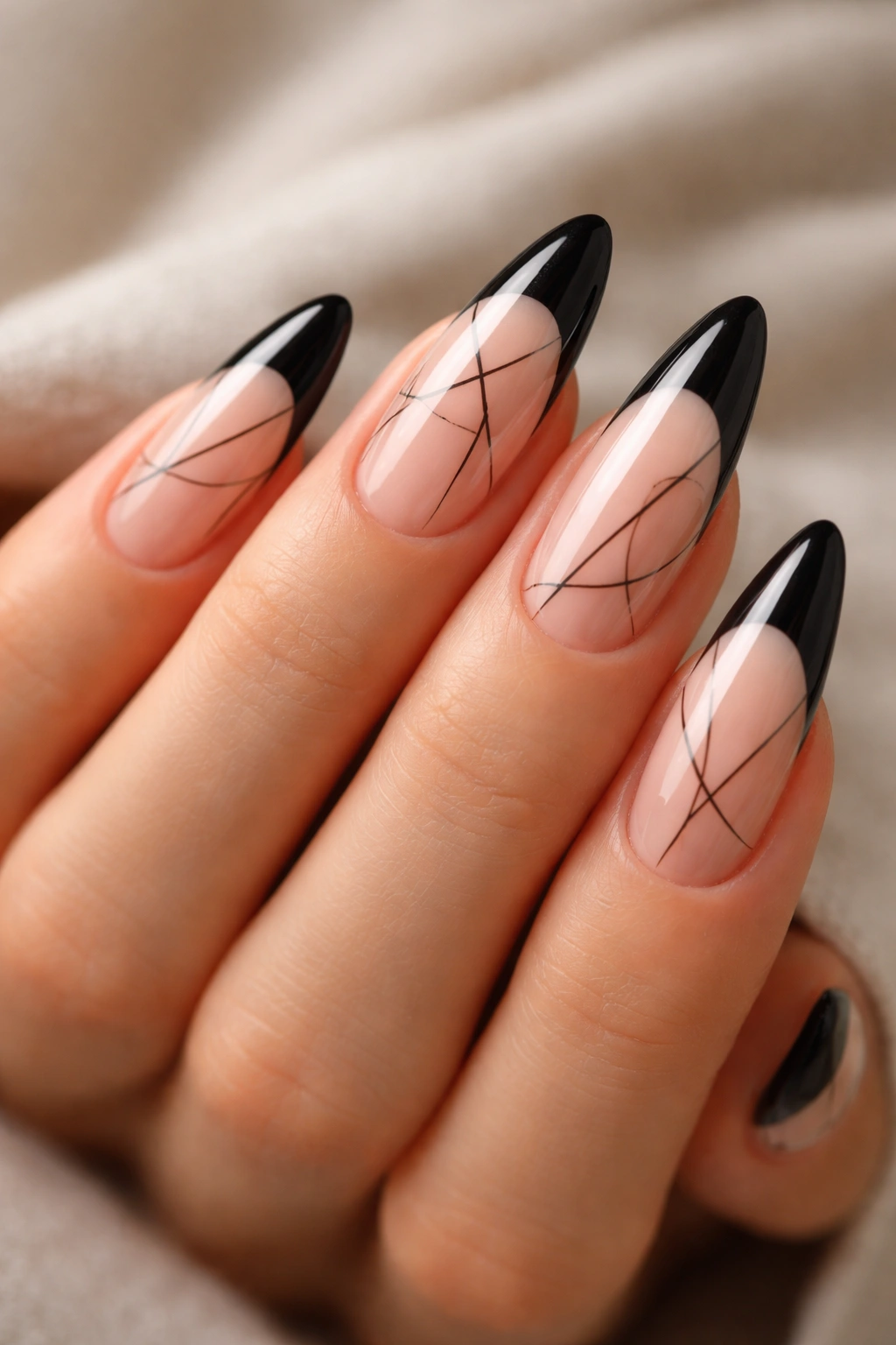 Close-up of long almond nails with black tips and abstract line art on nude bases.