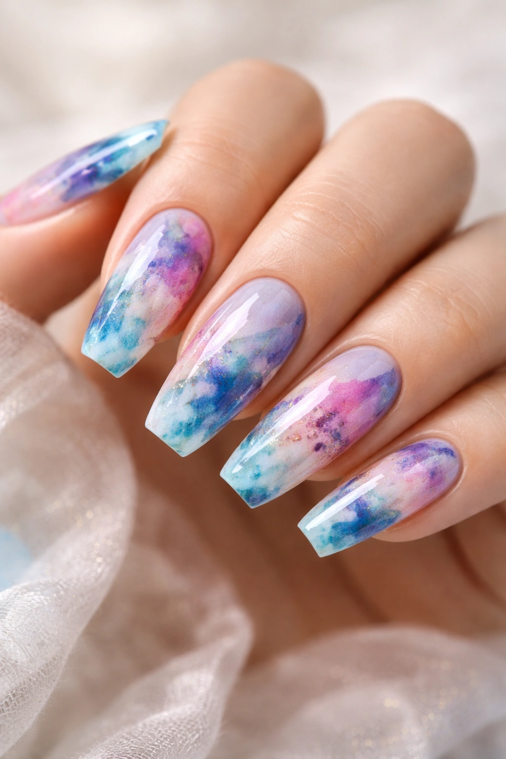 Close-up of curved coffin nails with abstract watercolor wash in blues and purples on medium-length nails