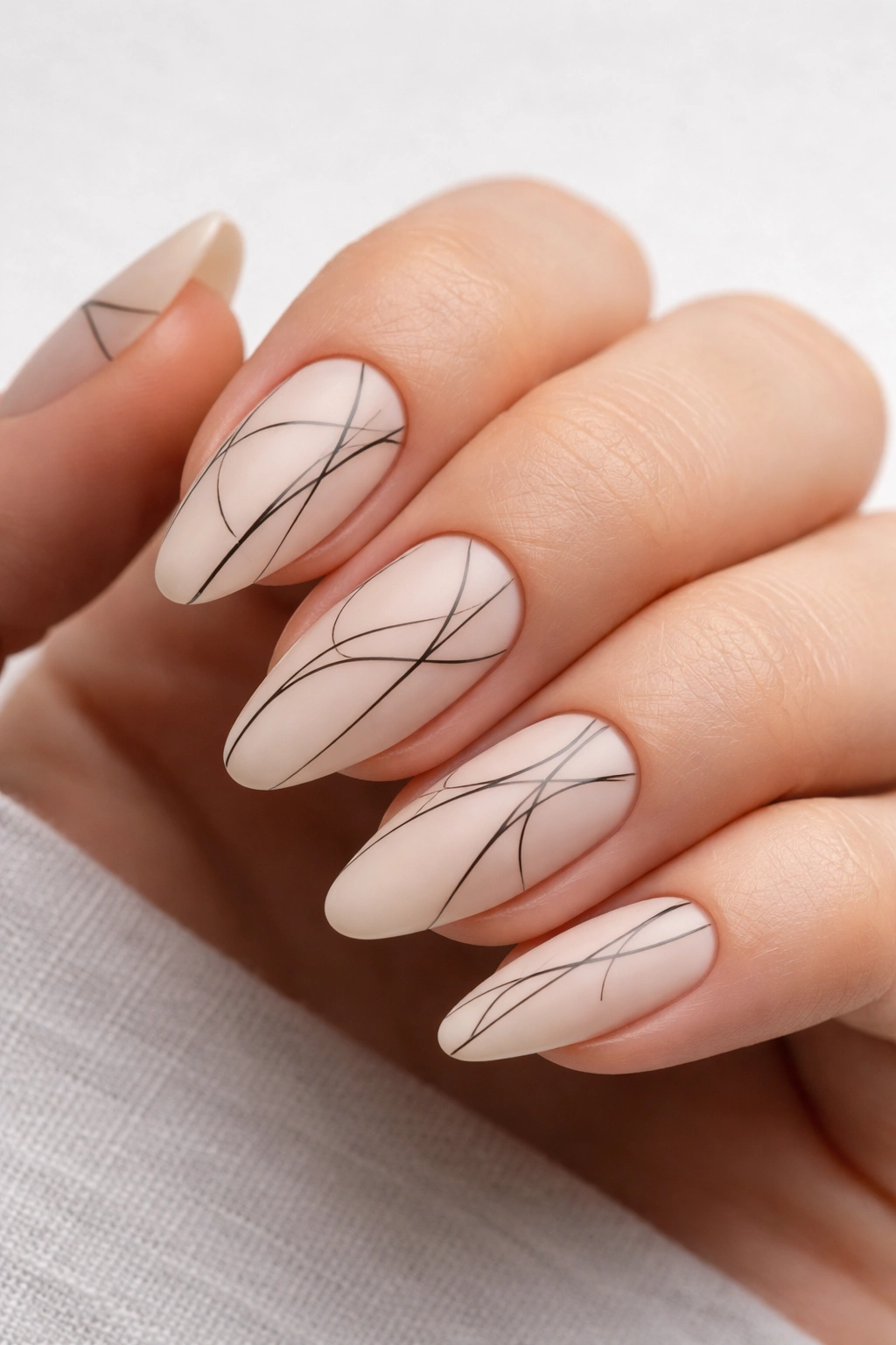 Close-up almond nails with abstract line art on sheer nude base