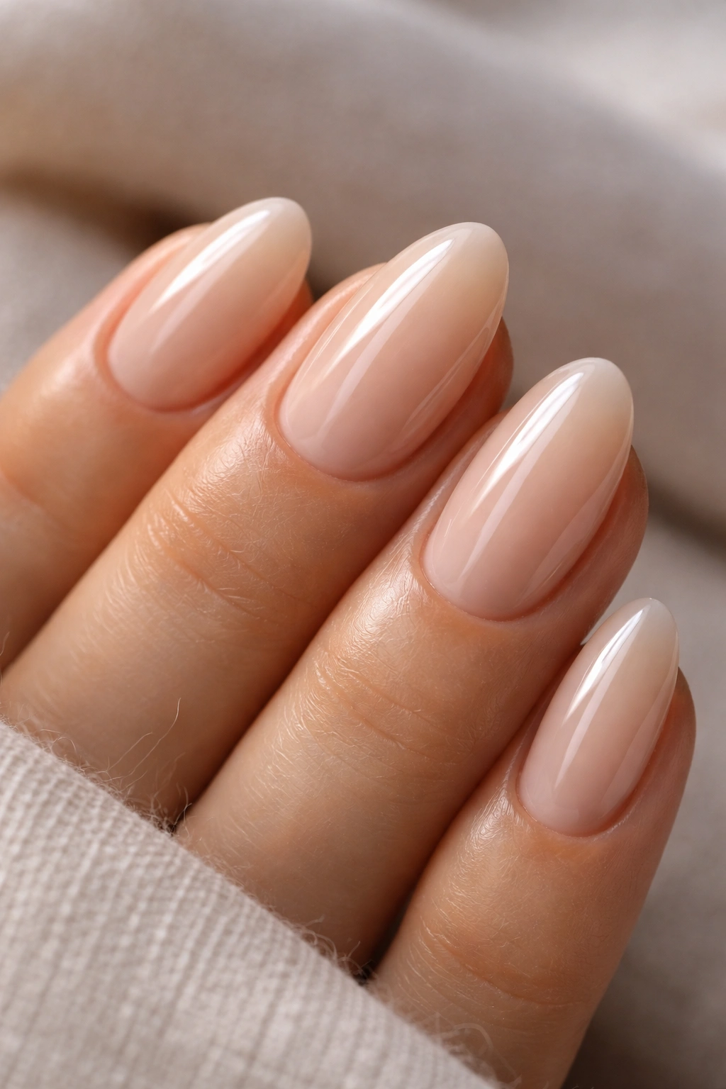 Close-up of short almond nails with sheer beige and glassy shine