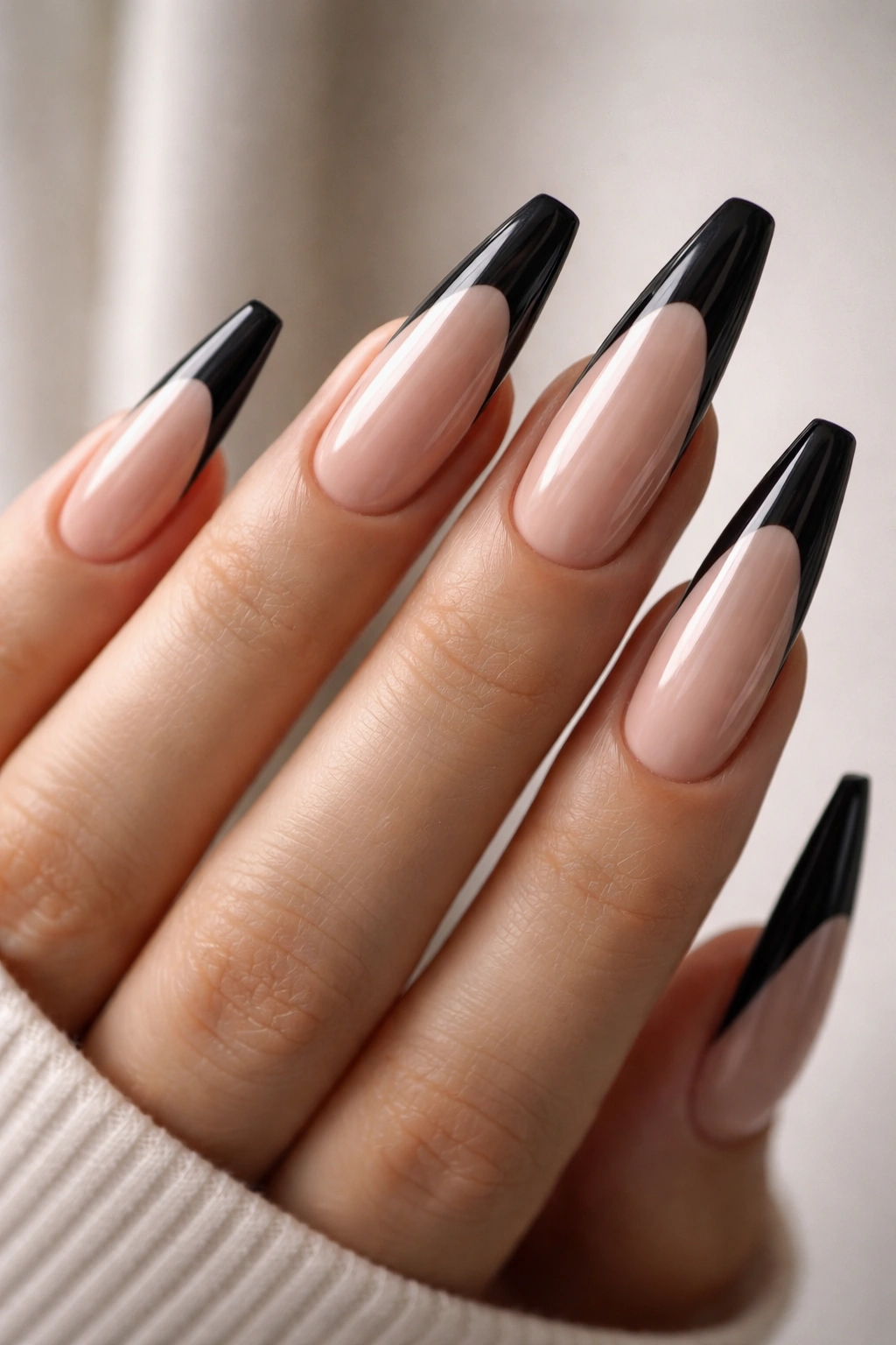 Close-up of extra-long almond coffin hybrid nails with black French tips on nude base