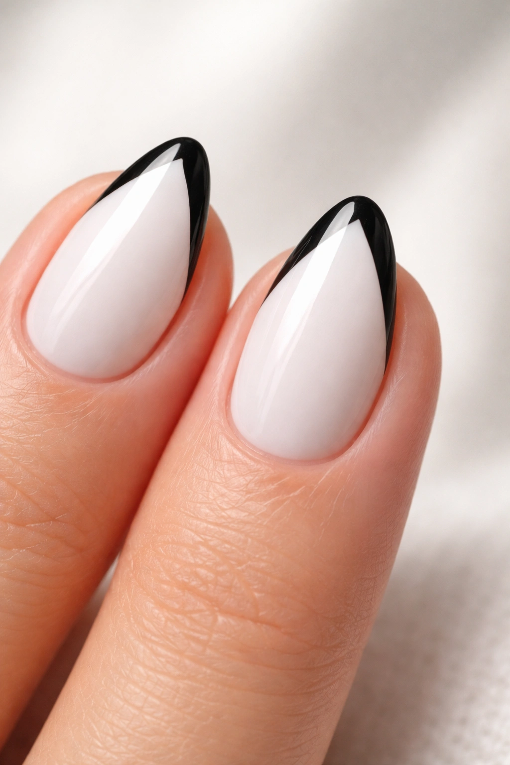 Close-up of short white almond nails with black V-tip accents.