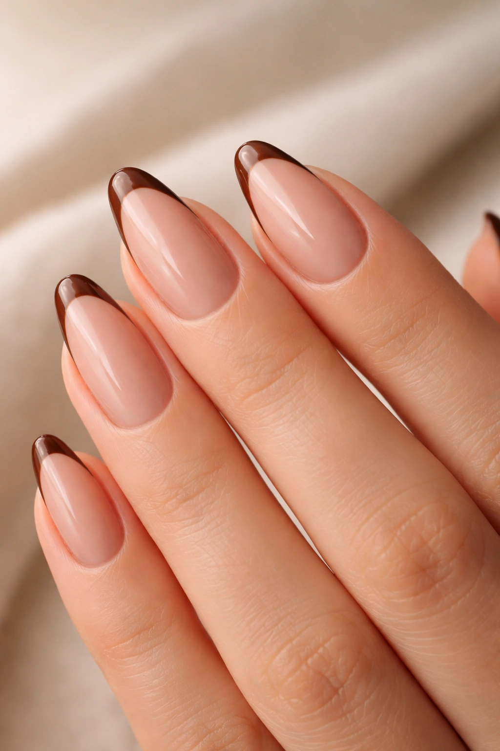 Close-up of almond nails with brown French tips on a pink nude base