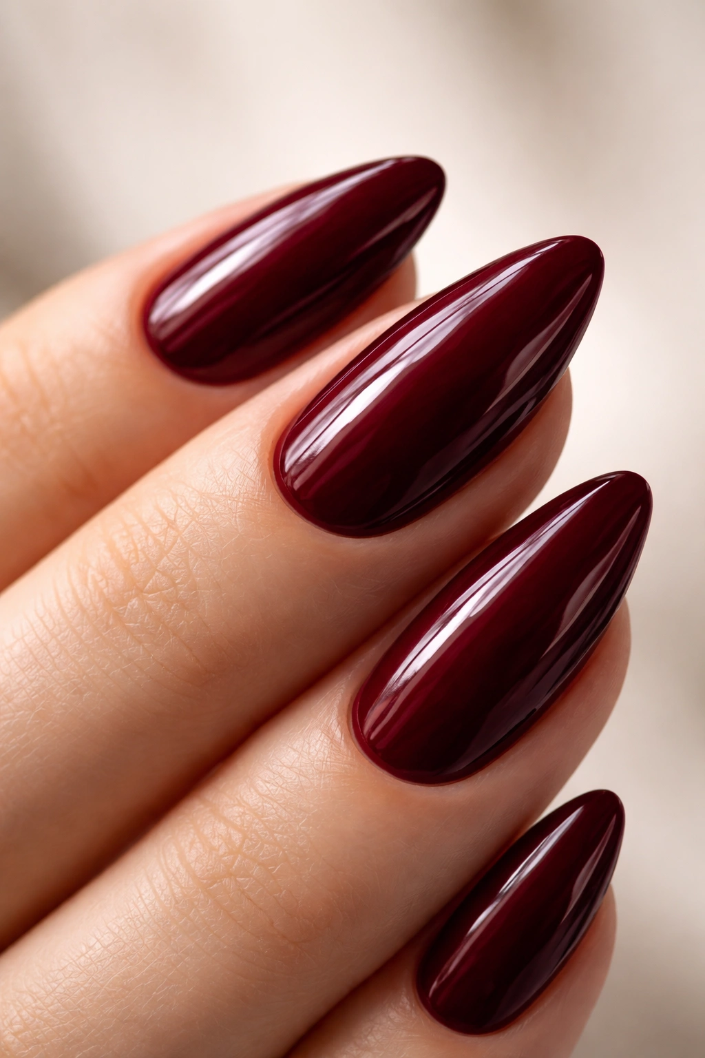Close-up of almond-shaped nails painted burgundy with high gloss