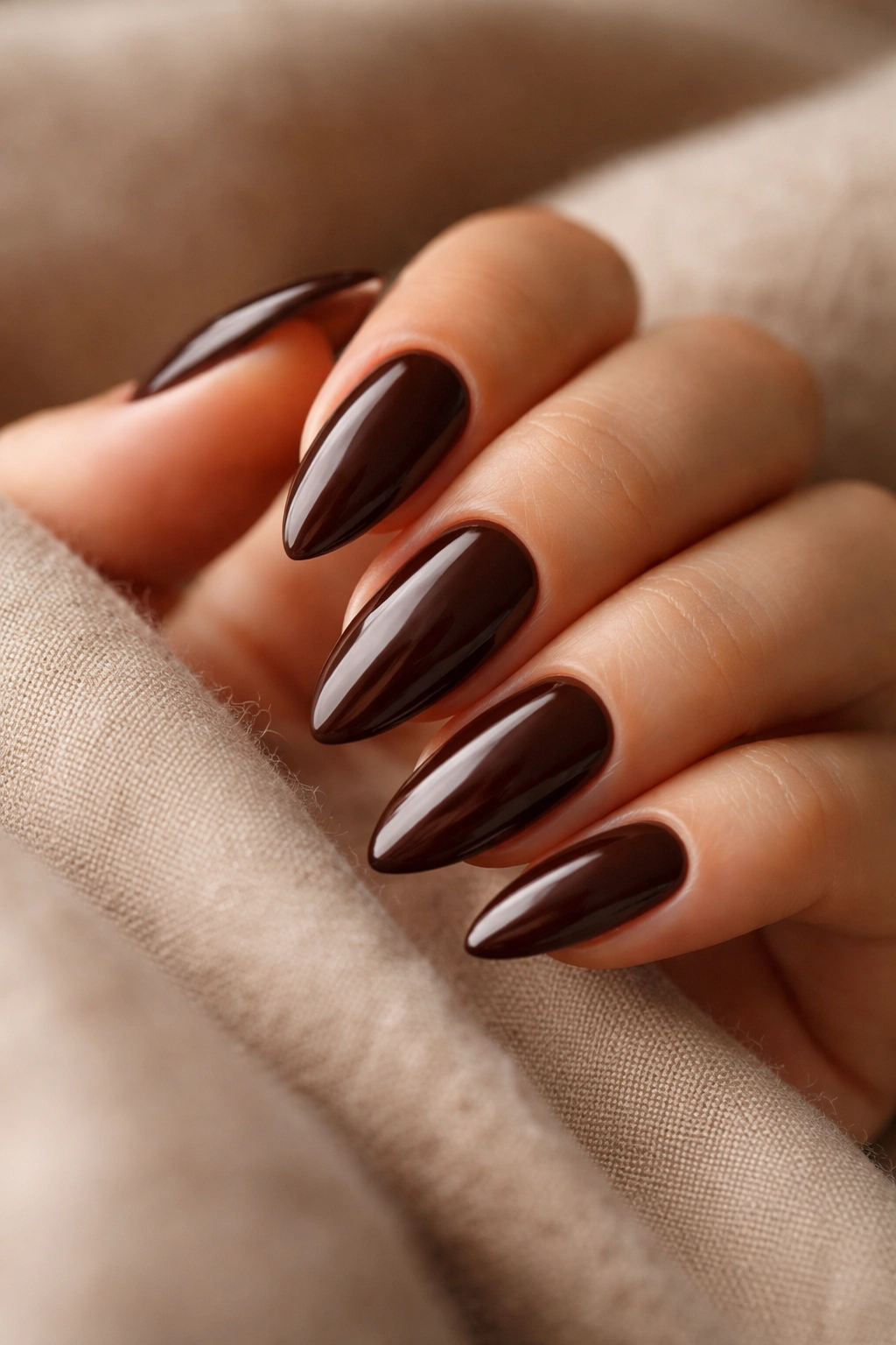 Close-up of glossy deep chocolate almond nails on a hand