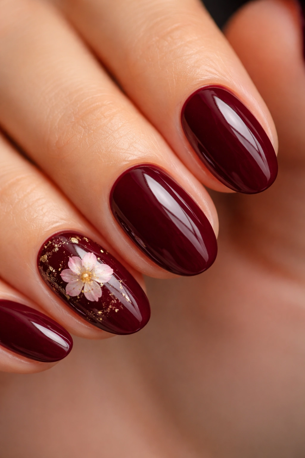 Short almond nails with a dark cherry base and a small pressed dried flower accent