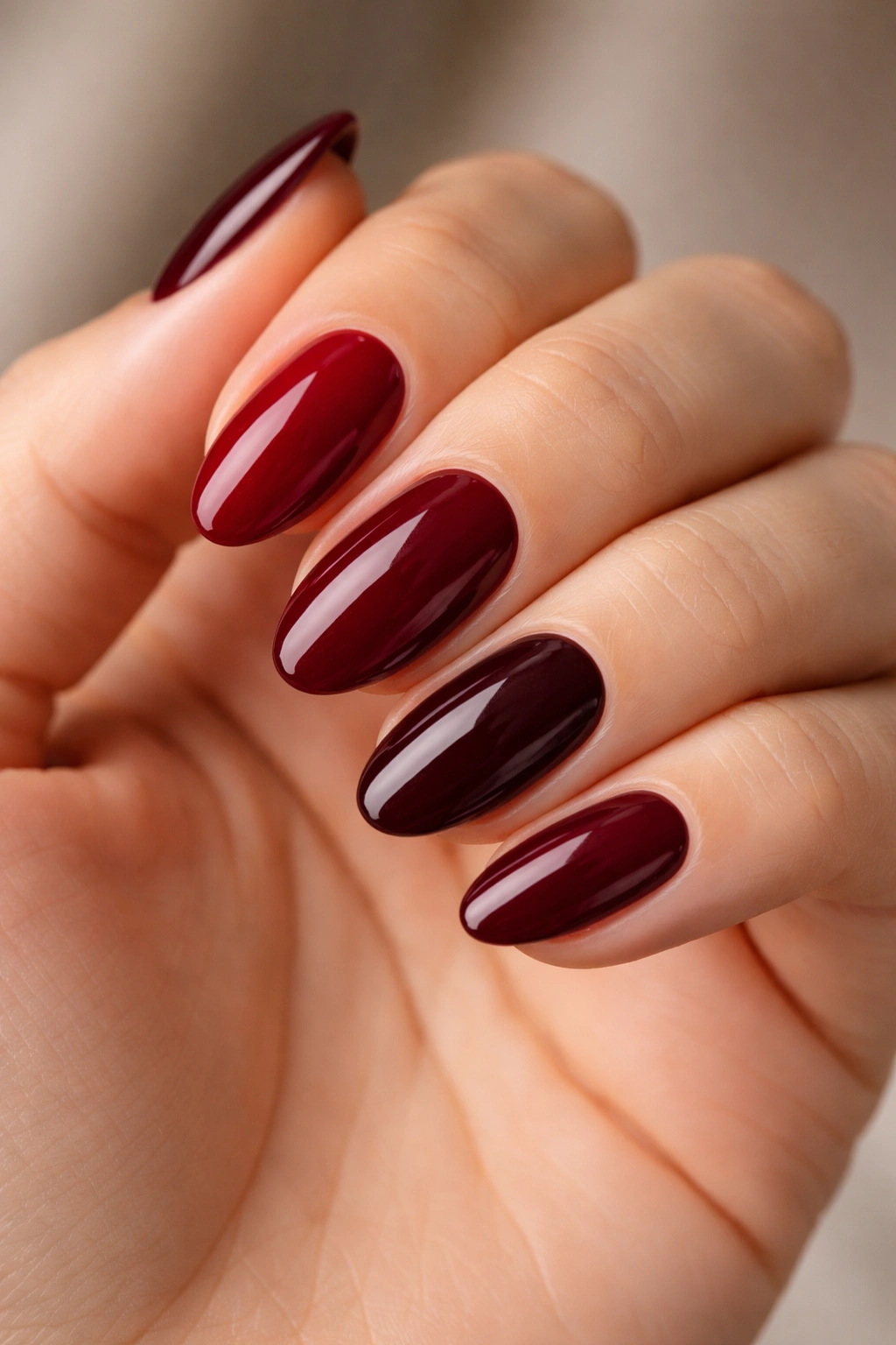Five almond nails painted in different dark red shades on a neutral background