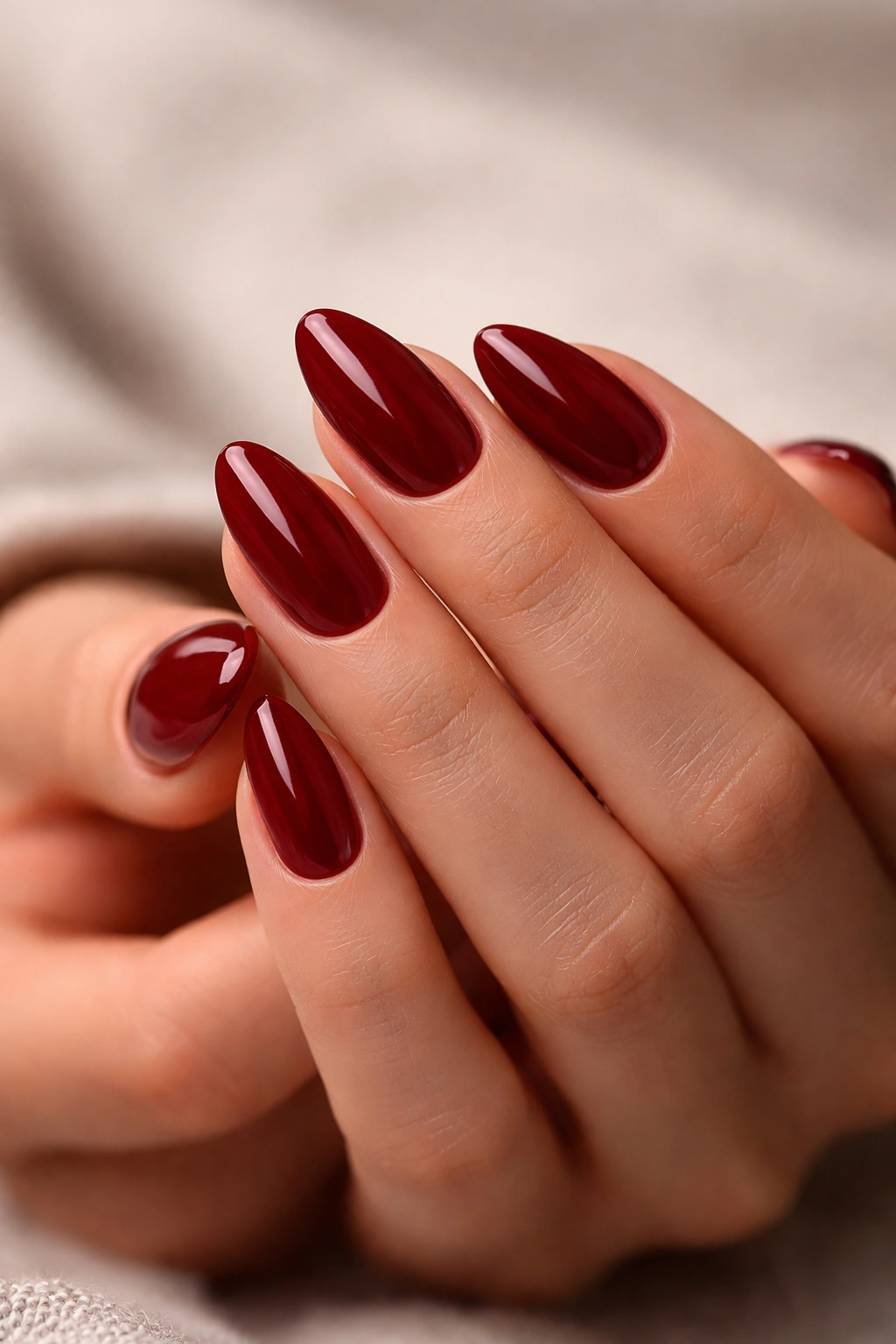 Close-up of almond nails in deep red with glossy finish.