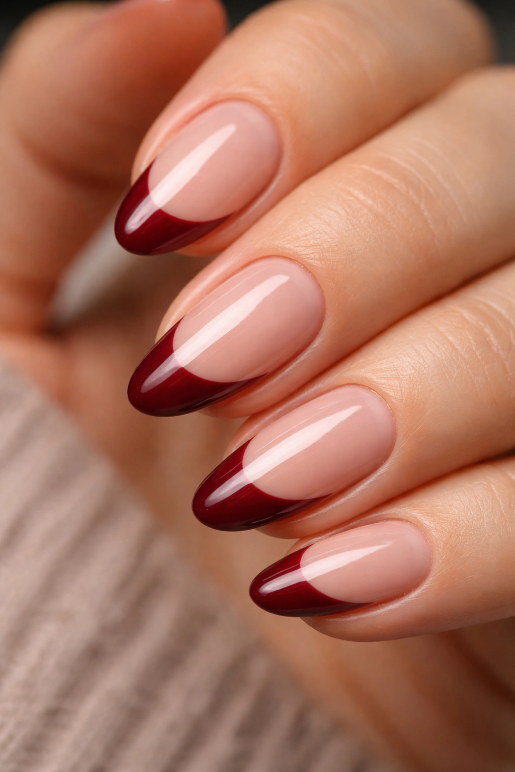 Almond nails with deep red French tips on a natural nude base, clean curve