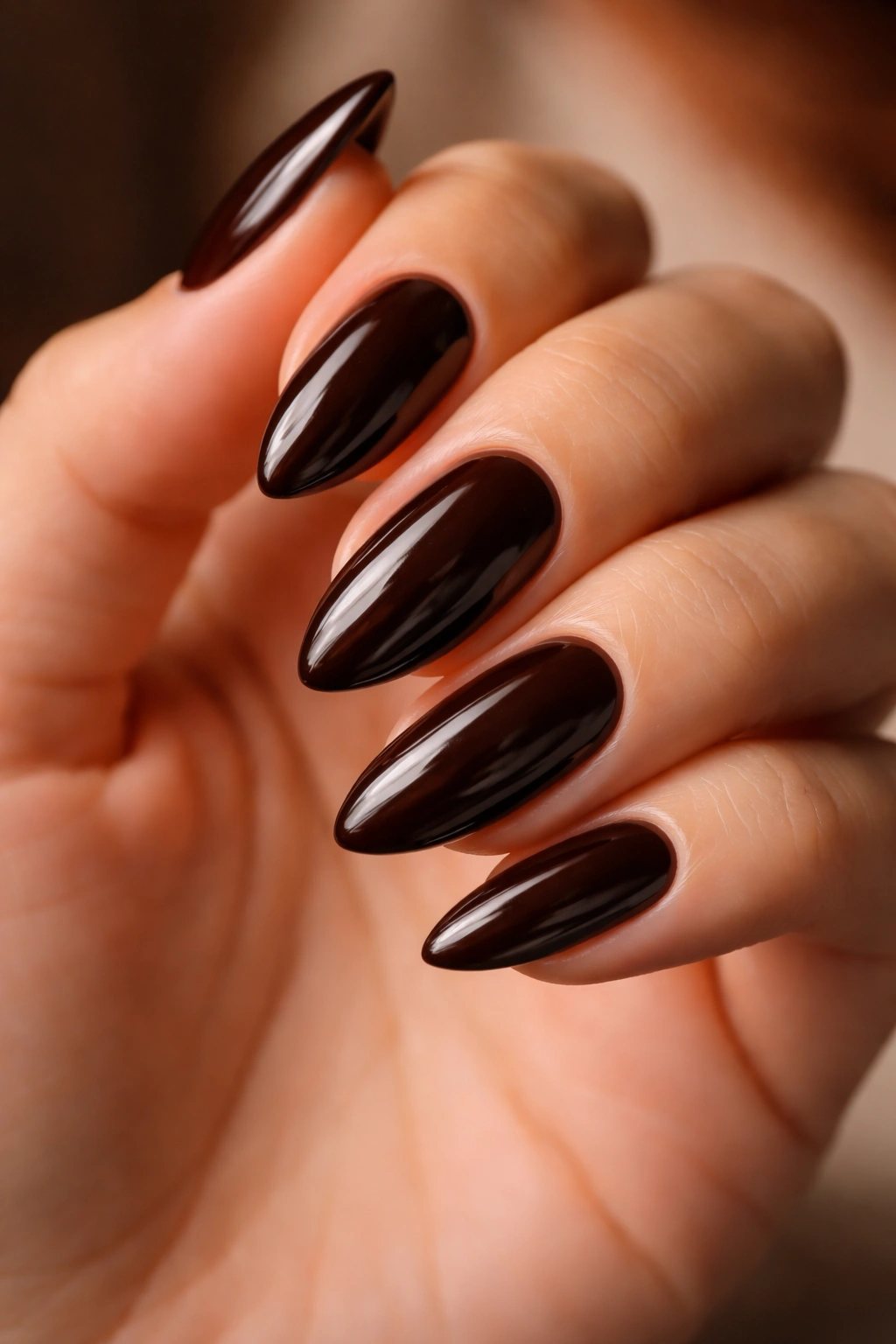 Close-up of deep espresso almond nails on a hand with a glossy finish