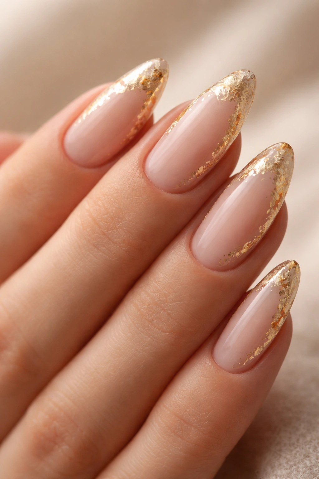 Close-up of almond nails with irregular gold foil on nude base