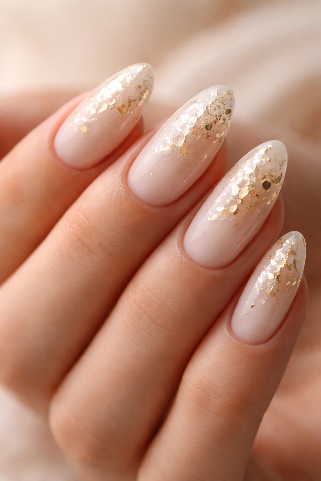 Milky almond nails with scattered gold foil in painterly pattern.