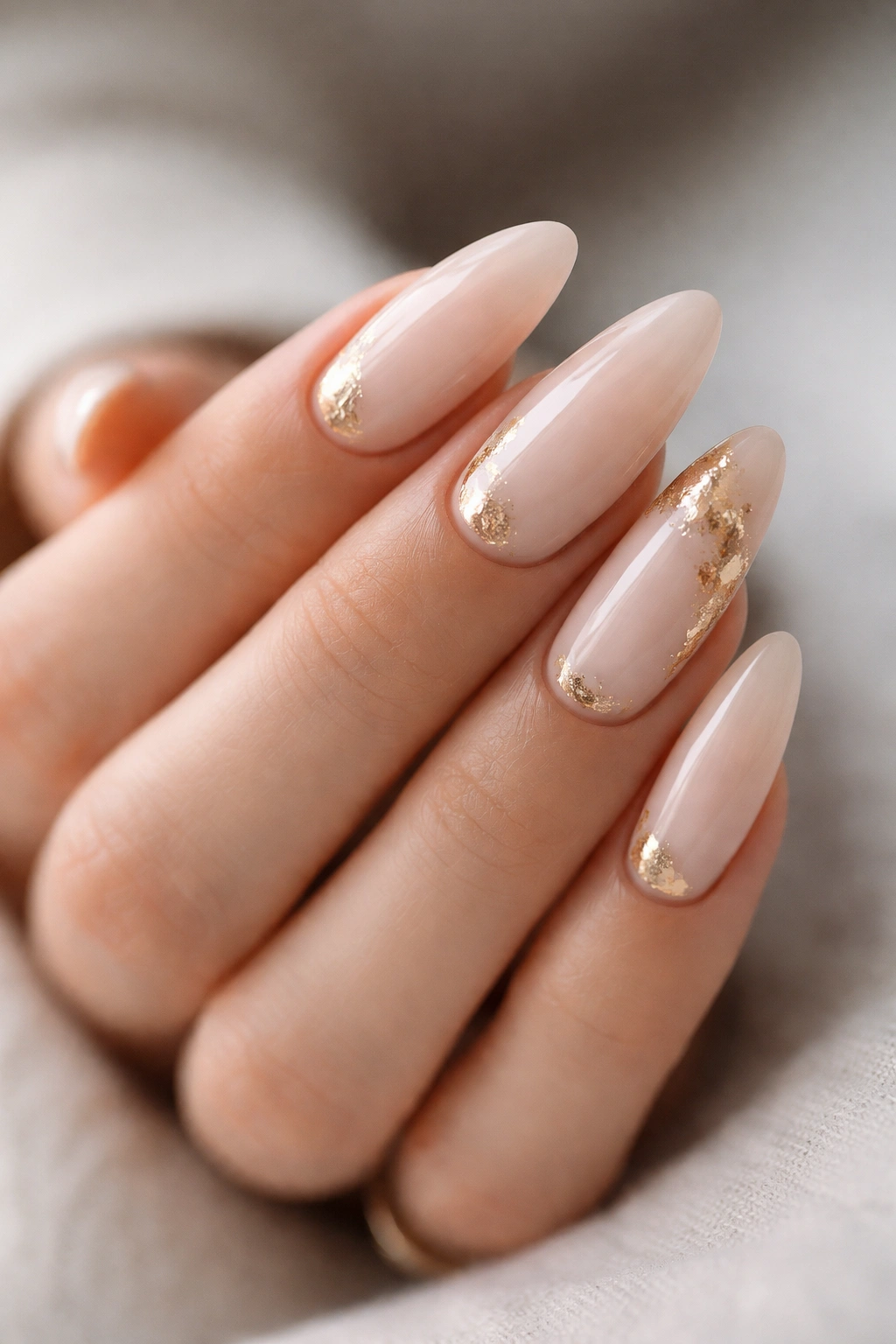 Close-up of almond nails with gold foil accents on a milky nude base