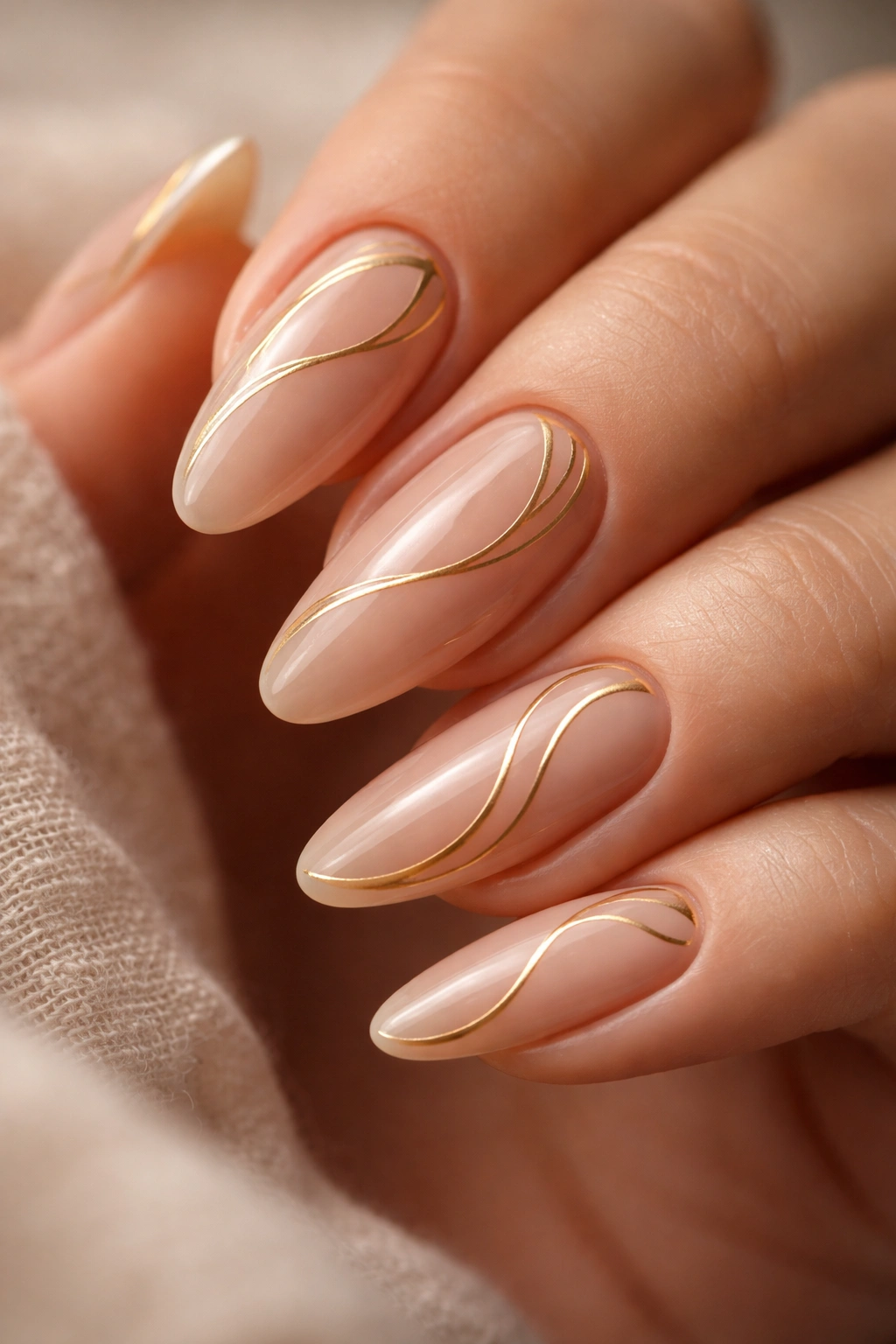 Nude almond nails with delicate gold swirls and negative space.
