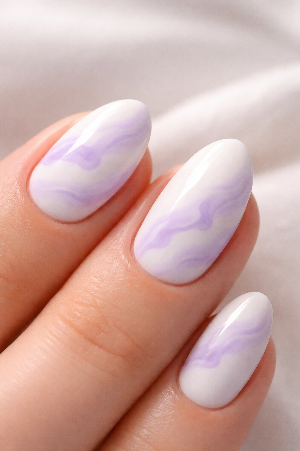 Close-up of white almond nails with lavender cloud swirl patterns.