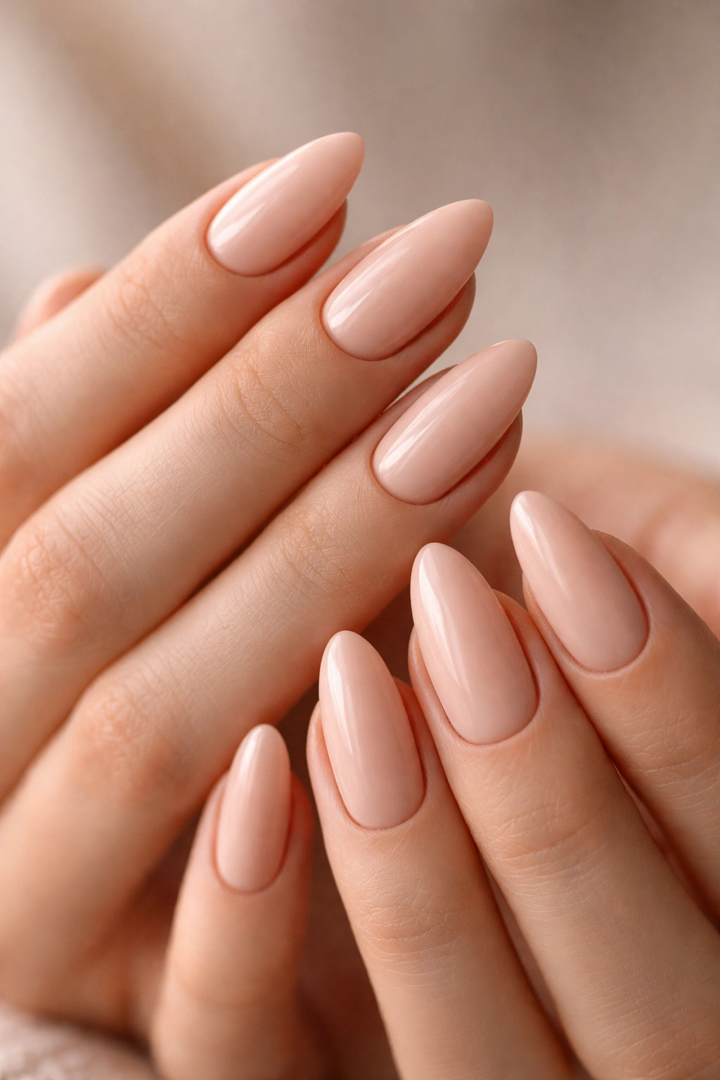 Close-up of almond nails in a soft beige-pink nude shade, smooth and polished.