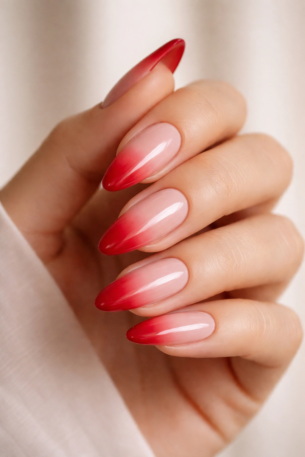 Close-up of almond nails with red ombré fade on nude base, studio lighting
