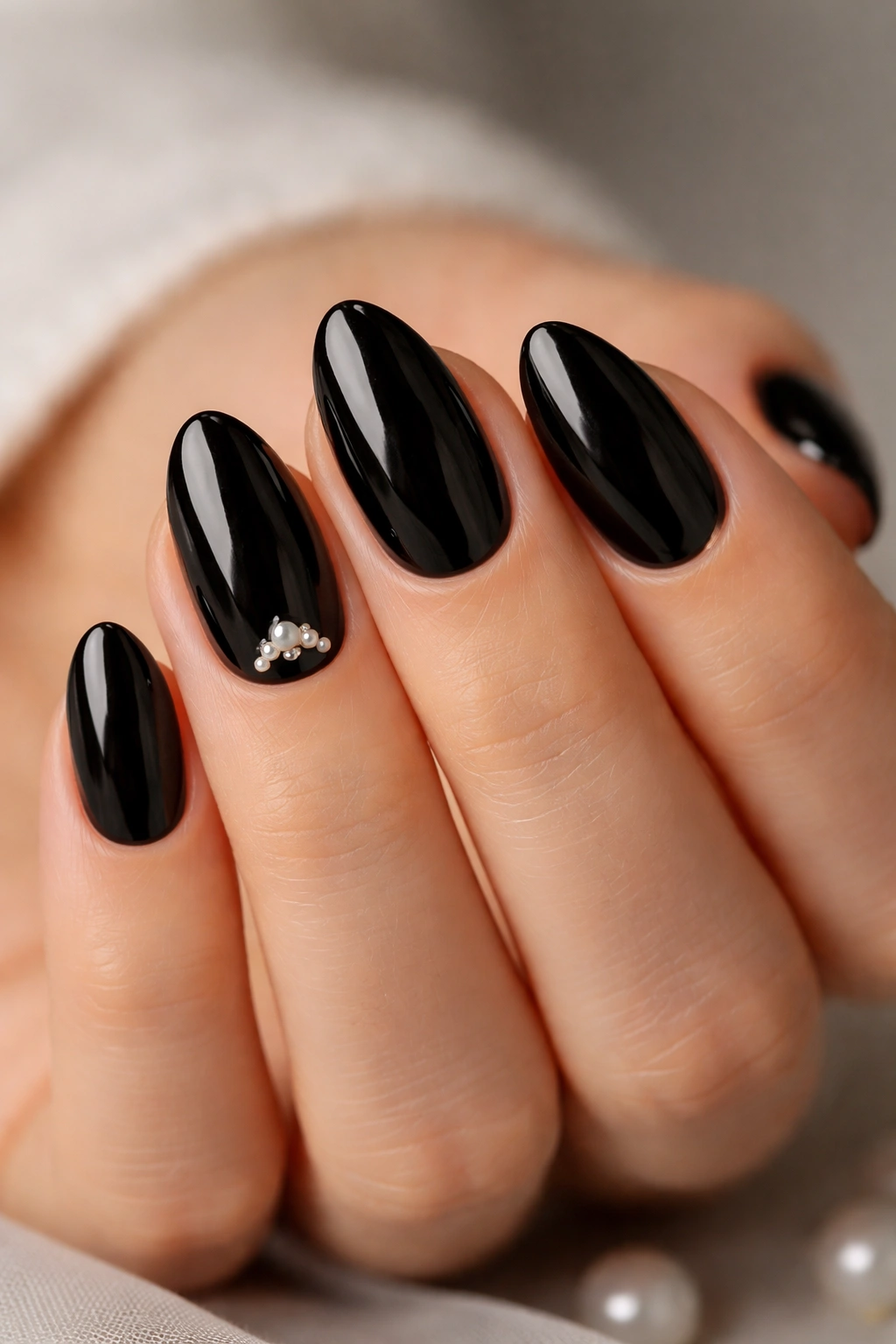 Close-up of short black almond nails with tiny pearls near the cuticle on a neutral background