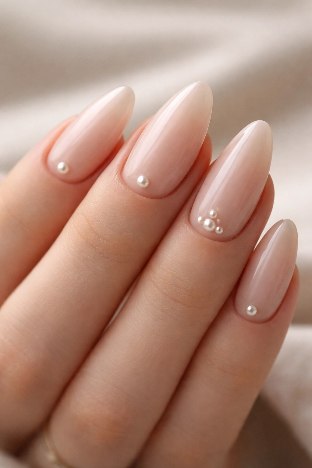 Close-up of almond nails with tiny pearl accents near the cuticle on a soft nude base