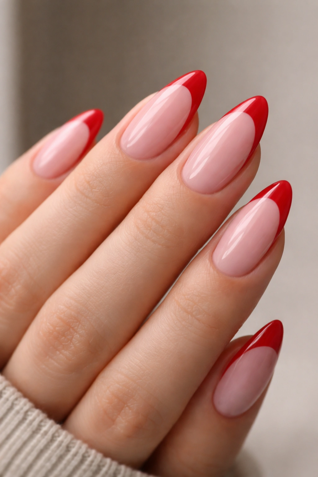 Almond nails with sheer pink base and red French tips on a neutral background