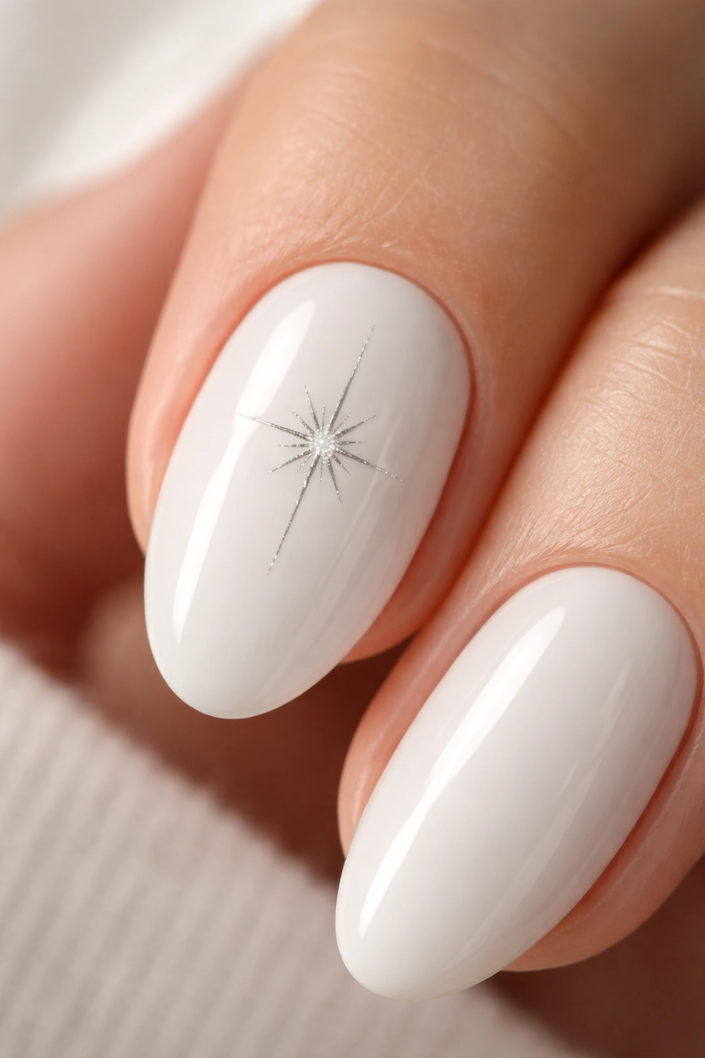 Close-up of a short white almond nail with a silver starburst accent.