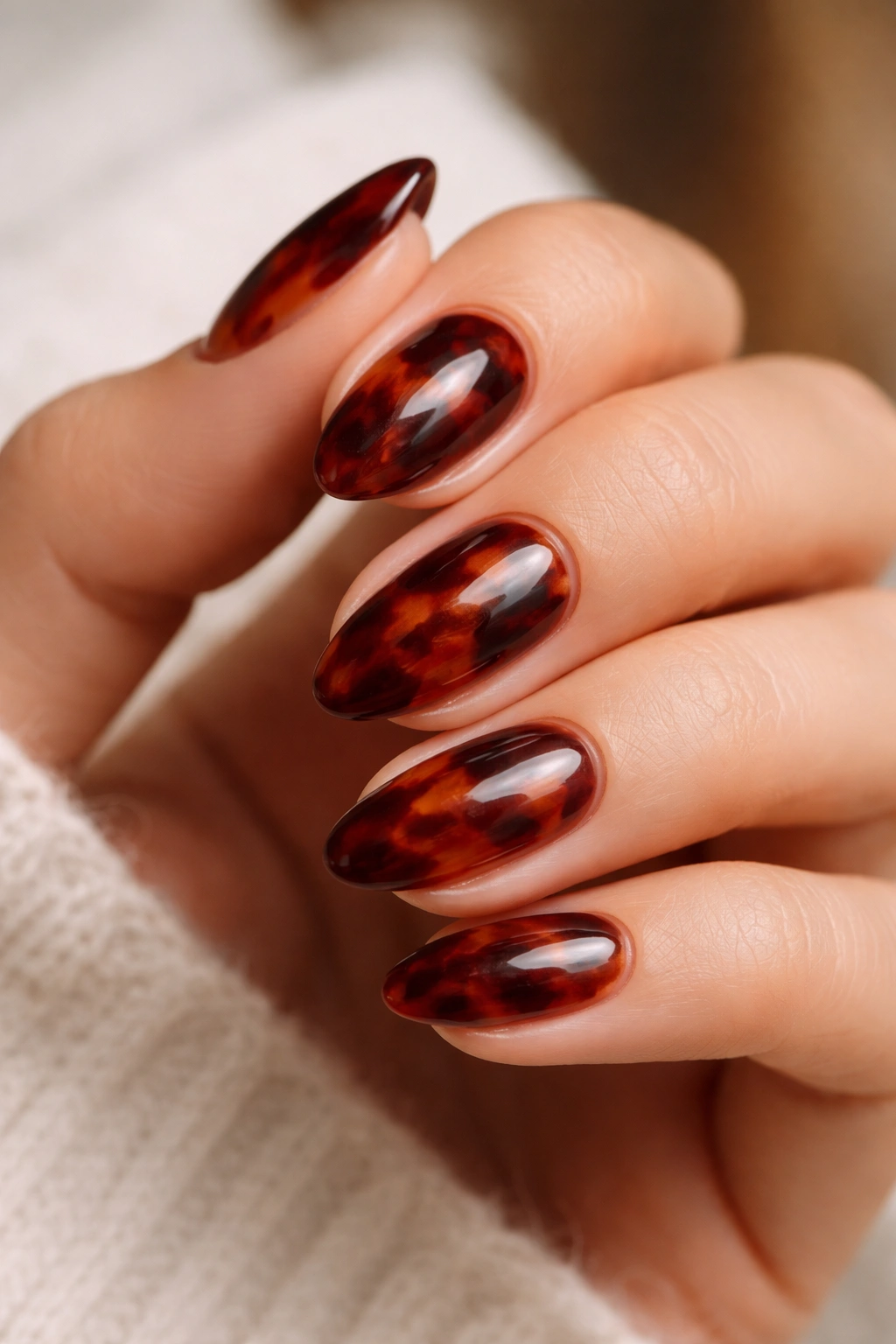 Almond nails with maroon tortoiseshell pattern on a nude base, studio lighting