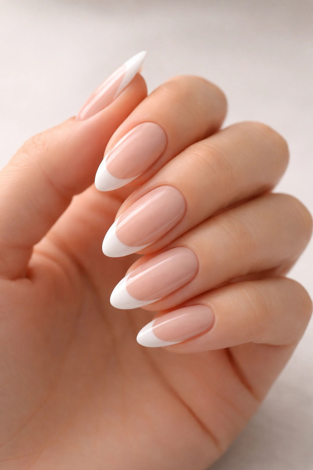 Close-up of soft almond nails with a slim white French tip on a nude milky-pink base