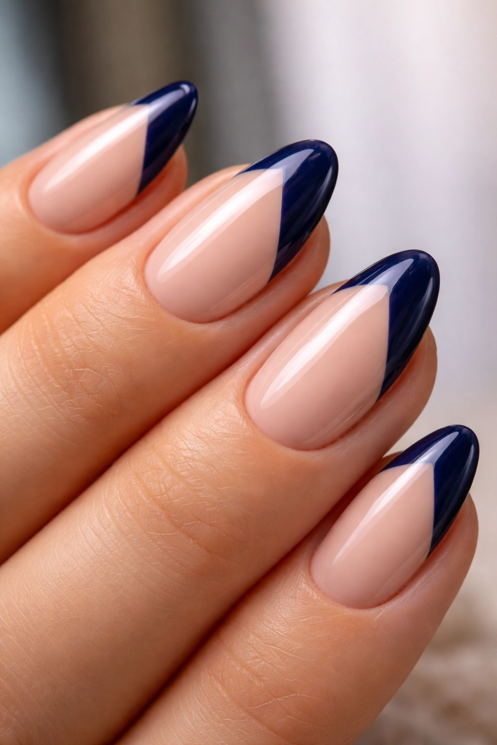 Close-up of almond nail with diagonal navy tip forming an inverted V on nude base