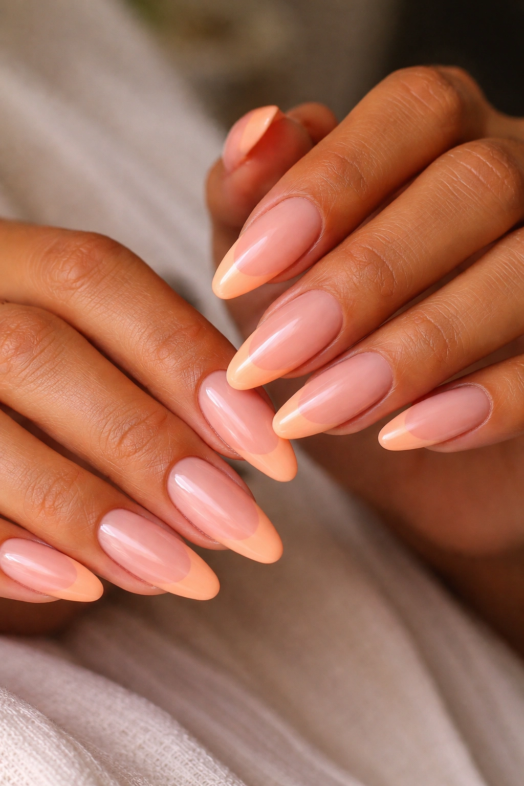 Apricot French tips on sheer nude base on warm-toned hands.