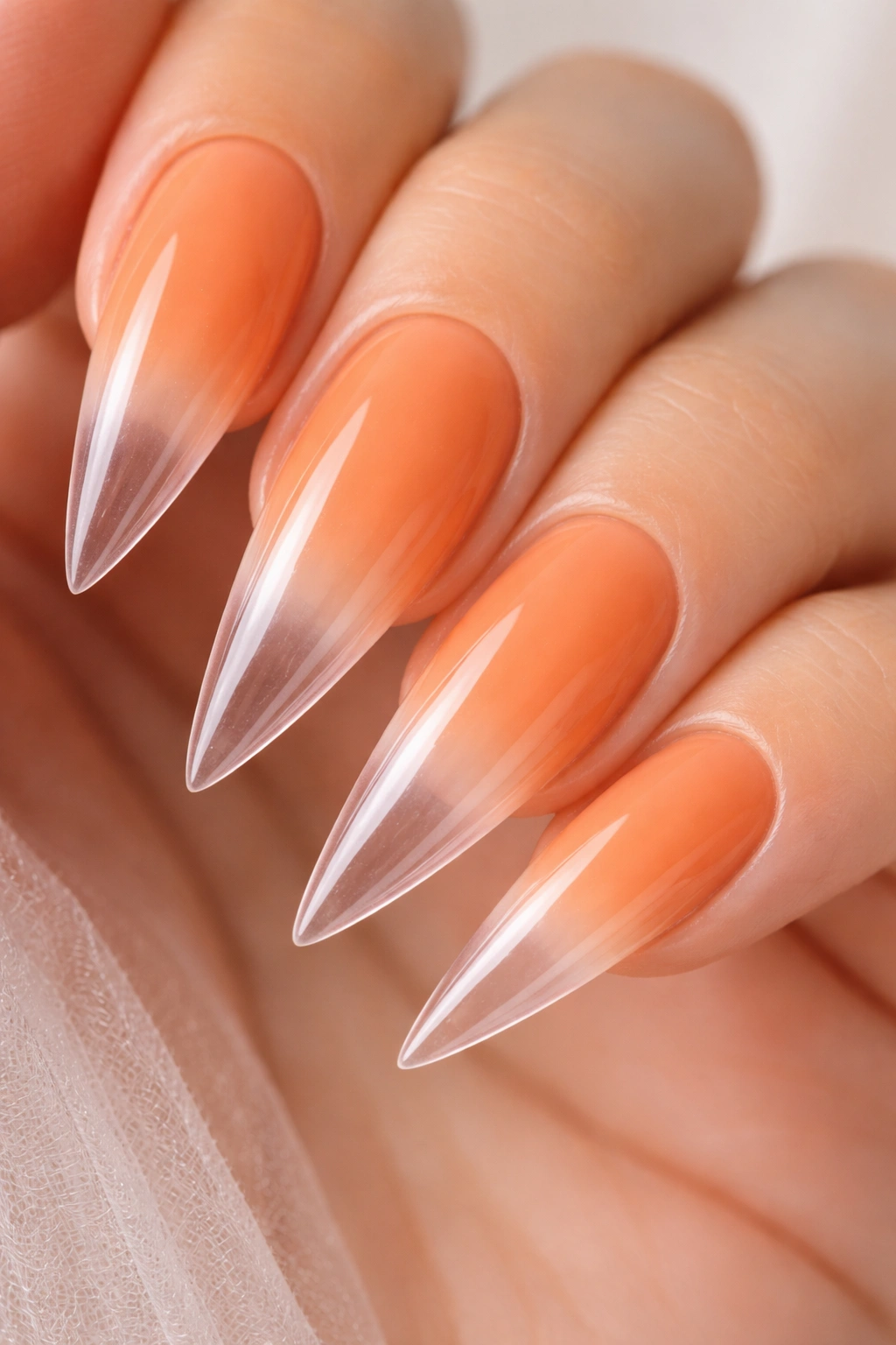 Close-up of apricot-orange gradient stiletto nails fading to clear tips