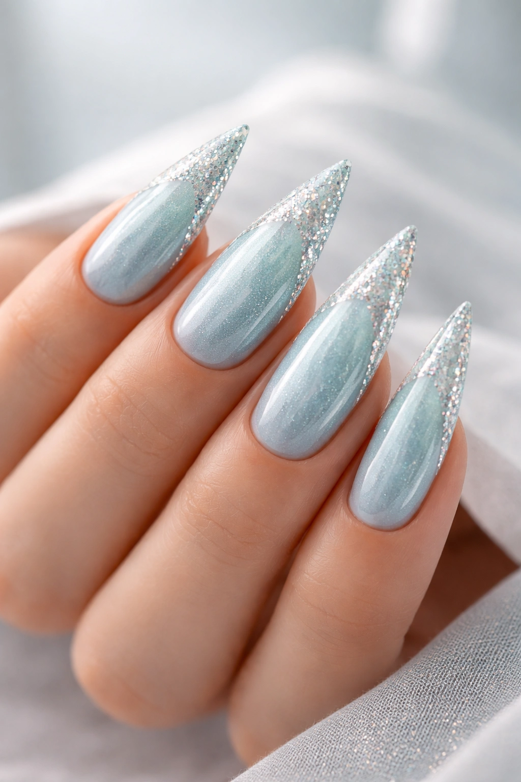 Close-up of a stiletto nail with aqua shimmer and glitter accents
