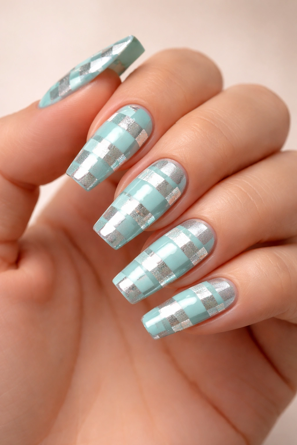 Close-up of aqua and silver checkerboard coffin nails on a hand with a neutral backdrop