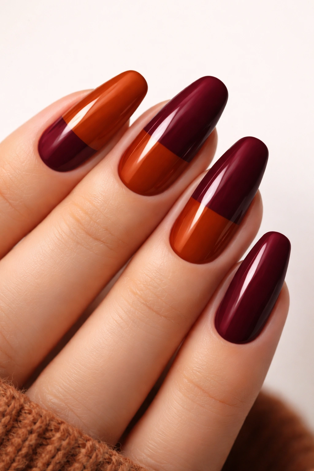 Nails with auburn and burgundy color-block design on a neutral background